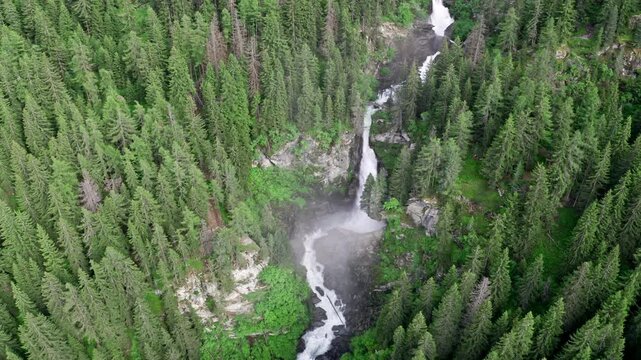 Cascate del rutor waterfall cascading through lush green forest in the alps, aerial view