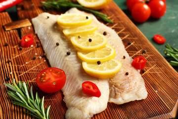Wooden board of raw codfish fillet with lemon on table