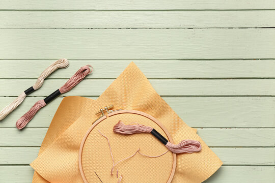 Wooden embroidery hoop with canvases, mouline threads and scissors on green wooden background