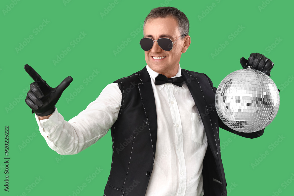 Poster Cool mature man in suit with disco ball pointing at something on green background