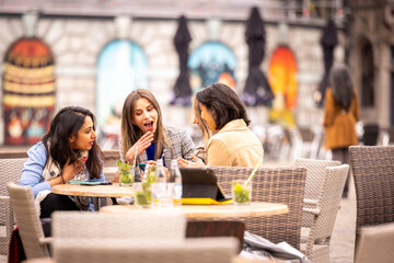 Three women seated at an outdoor caf table, engaged in lively conversation with drinks