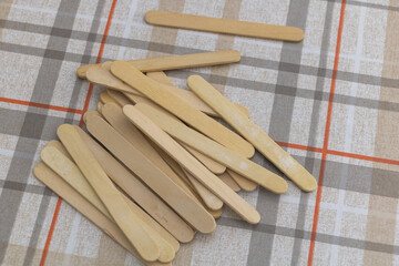 A pile of wooden popsicle sticks on top of an elegant checkered tablecloth, ready to be used for crafting or serving ice cream