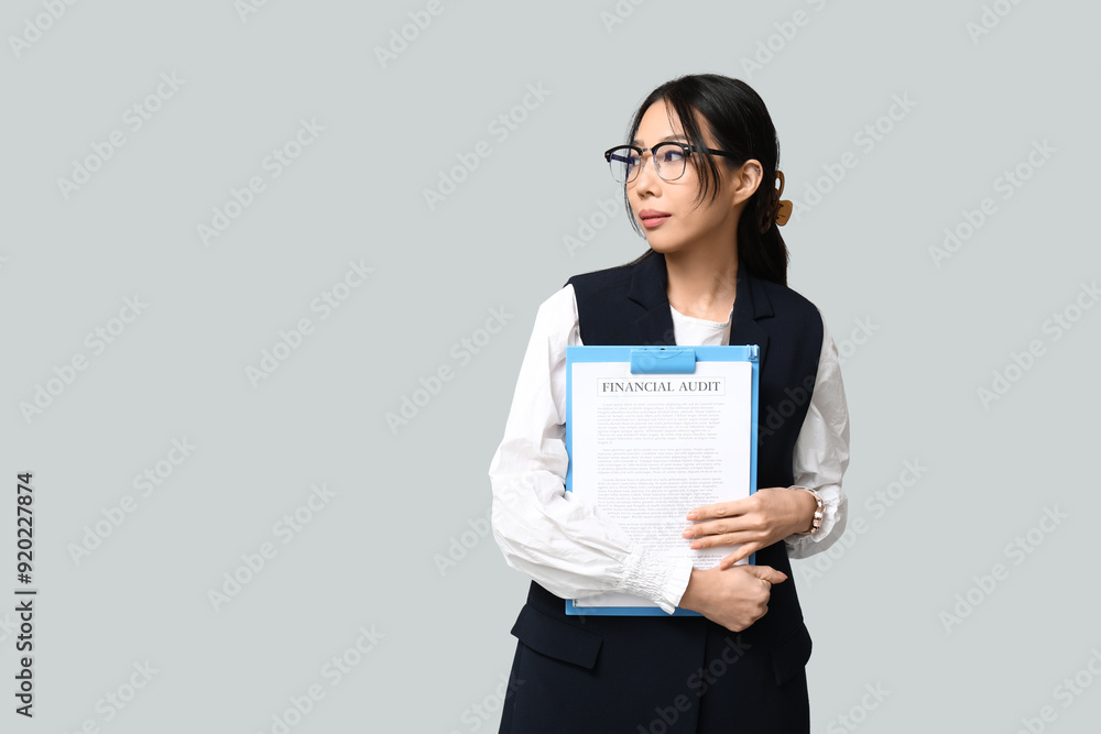 Wall mural Portrait of young Asian businesswoman with clipboard on grey background