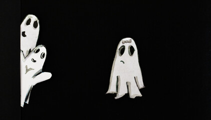 Mischievous ghosts peeking out from behind a wall.Black background.