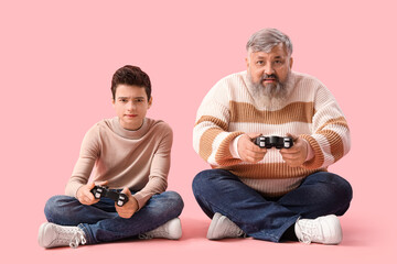 Happy grandfather with his cute grandson playing video games on pink background