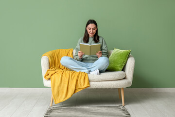 Young woman reading book on sofa in green living room