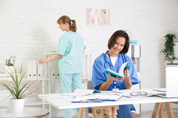 Female medical intern with copybook studying at table in clinic