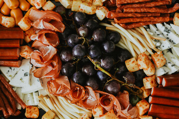 macro shooting of various snacks in the form of meats and cheeses with grape on a black plate 