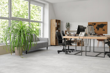 Interior of stylish office with grey sofa, workplace, modern computer and armchairs