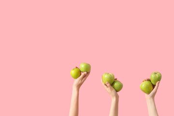 Hands with fresh green apples on pink background