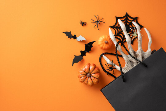 Halloween themed flat lay with pumpkins, black bats, spiders, and shopping bag on an orange background