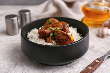 Delicious sweet and sour chicken with rice in black bowl on grey grunge background