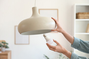 Young woman screwing light bulb into ceiling lamp at home, closeup