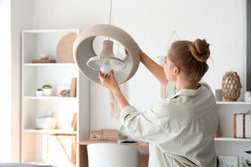 Young woman screwing light bulb into hanging lamp at home