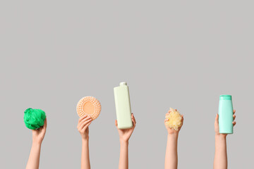 Female hands with bottles of cosmetic products and bath sponges on grey background