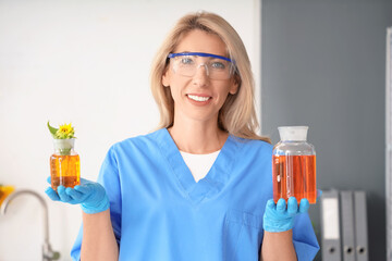 Happy female scientist with flasks of samples and sunflower in laboratory