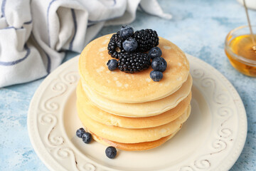 Plate of sweet pancakes with fresh blueberries, blackberries and bowl of honey on light blue background