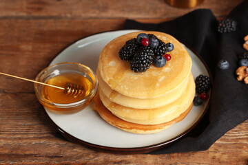 Plate of sweet pancakes with fresh berries and bowl of honey on wooden background