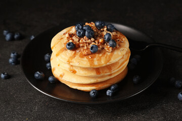 Plate of sweet pancakes with fresh blueberries and nuts on black background