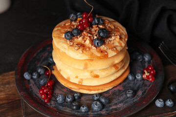 Plate of sweet pancakes with fresh berries and nuts on black background