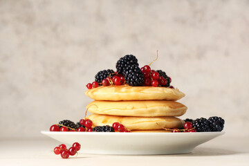Plate of sweet pancakes with fresh blackberries and red currants on white background