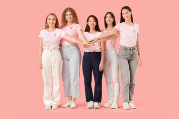 Obraz premium Beautiful women with pink ribbons putting hands together on color background. Breast cancer awareness concept