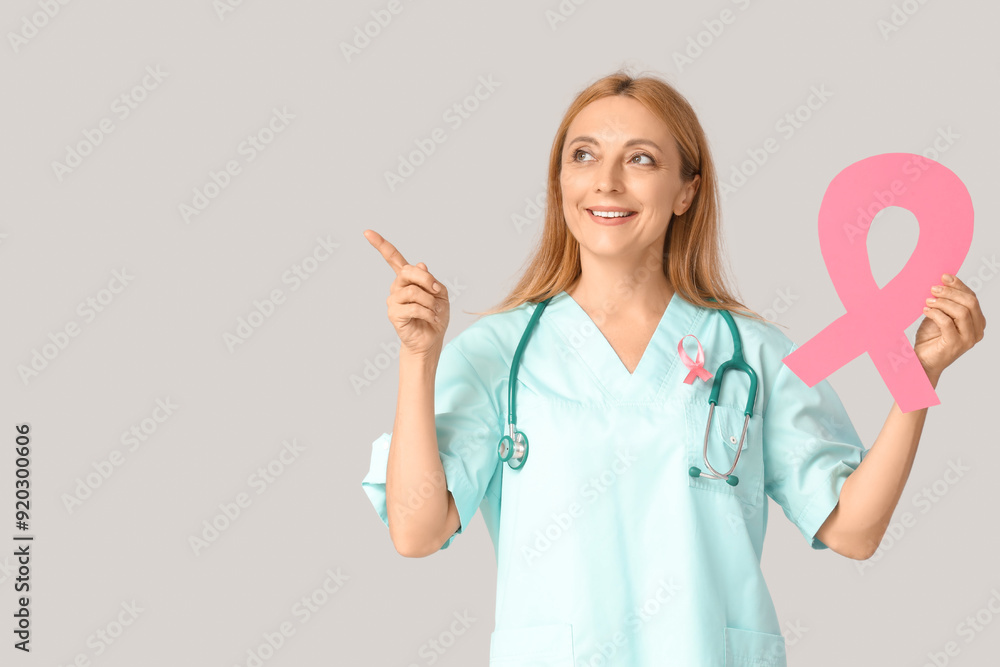 Sticker Female doctor with pink ribbons pointing at something on light background. Breast cancer awareness concept