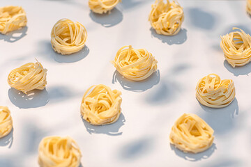 Nests of uncooked Italian Fettucine pasta arranged on table in sunlight with soft shadows.