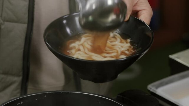 우동 사리가 든 그릇에 국자로 국물을 담는 모습