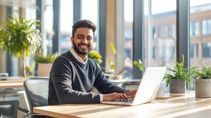 Smiling Young Indian Businessman Working on Laptop in a Bright Modern Office