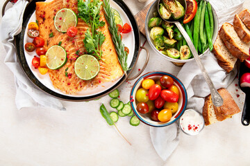 Grilled salmon and vegetables on wooden light background. Dinner table with cooked fish, tomatoes, asparagus