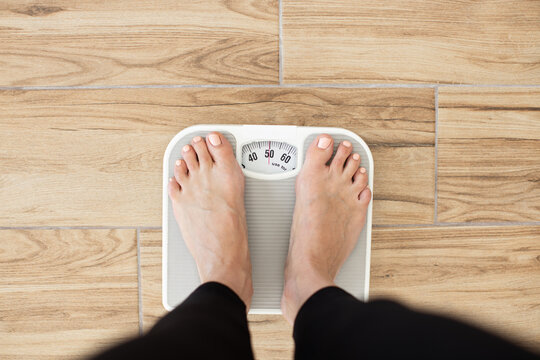 Person standing on scale measuring weight on wooden floor. Health and fitness concept focusing on weight management and wellness.