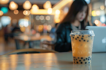 Iced bubble tea beverage drink with straw on cafe restaurant table with woman working on laptop on background. Co-working cafe place to work for freelancer relaxing summer altosphere concept. 