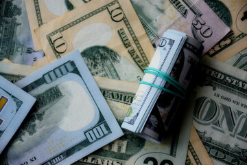 Hundred dollar bills roll lies on big amount of US dollars in different nominations under natural light