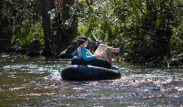 Boy leisurely tubing down a creek, surrounded by trees and sunlight.