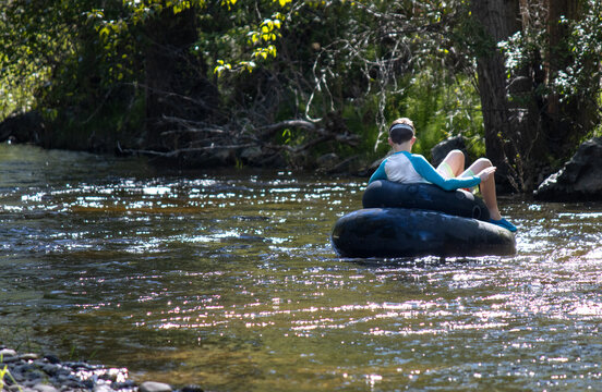 Boy leisurely floating down a creek on a tube, surrounded by forest.