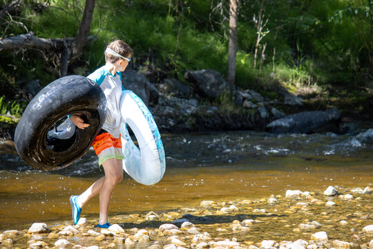 Boy carrying two tubes, walking across a rocky riverbank