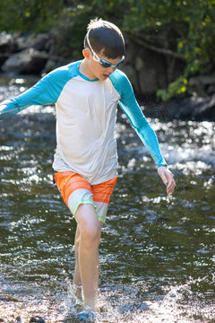 Boy wading through a creek after tubing, wearing swimwear and goggles