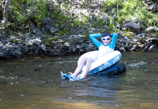 Boy relaxing while tubing down a creek, smiling and enjoying the wate