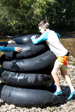 Boy stacking large tubes on a rocky riverbank while tubing down creek
