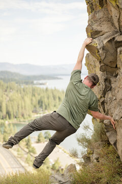 Male holding on with one hand on the side of a cliff
