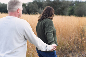 Couple holding hands while walking through a field of tall gras