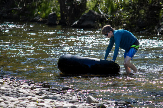 Boy in a shallow part of creek while adjusting an inflatable tube