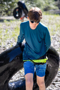 Boy tubing in a creek, holding an inflatable tube and wearing goggles