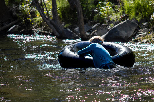 Boy floating on an inflatable tube in a shaded, forested area