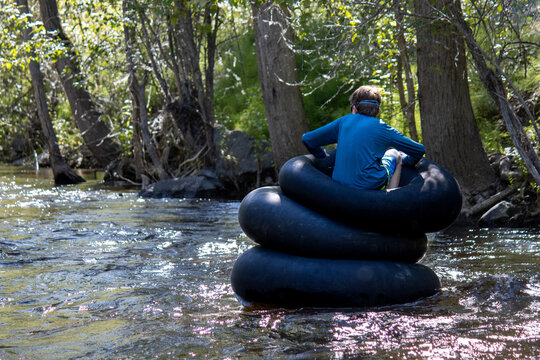 Boy floating on stacked inflatable tubes, surrounded by trees