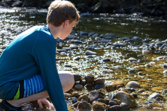 Boy crouching by a creek, playing with the rocks and water