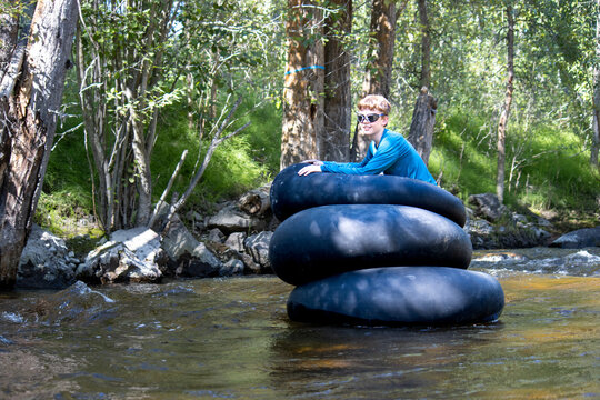 Boy enjoying a tubing adventure in a creek, sitting on stacked tubes