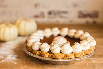 A pumpkin pie topped with whipped cream swirls, set on a wooden
