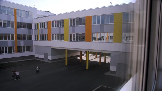 Large window of classroom provides charming view of schoolyard. Students dressed in uniform walk to school and discuss plans for day